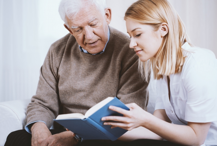 Caregiver reading book to senior man