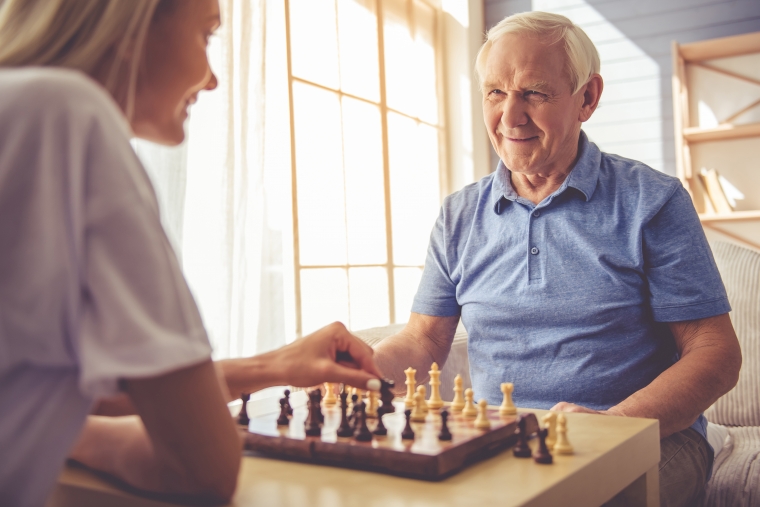 elderly man playing chess with his caregiver